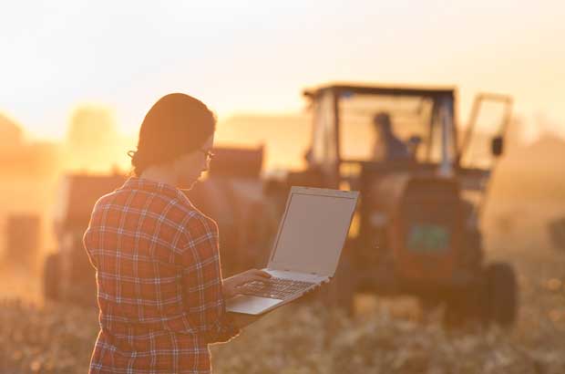 Woman with laptop and tractor in farm field