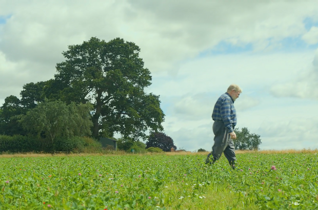 Farmer walks across field under grey and blue skies