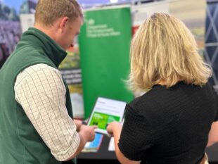 Engagement team member shows farming podcast to event attendee 