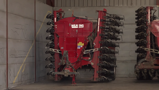 A direct drill, red in colour situated in farm building with grey floors and walls